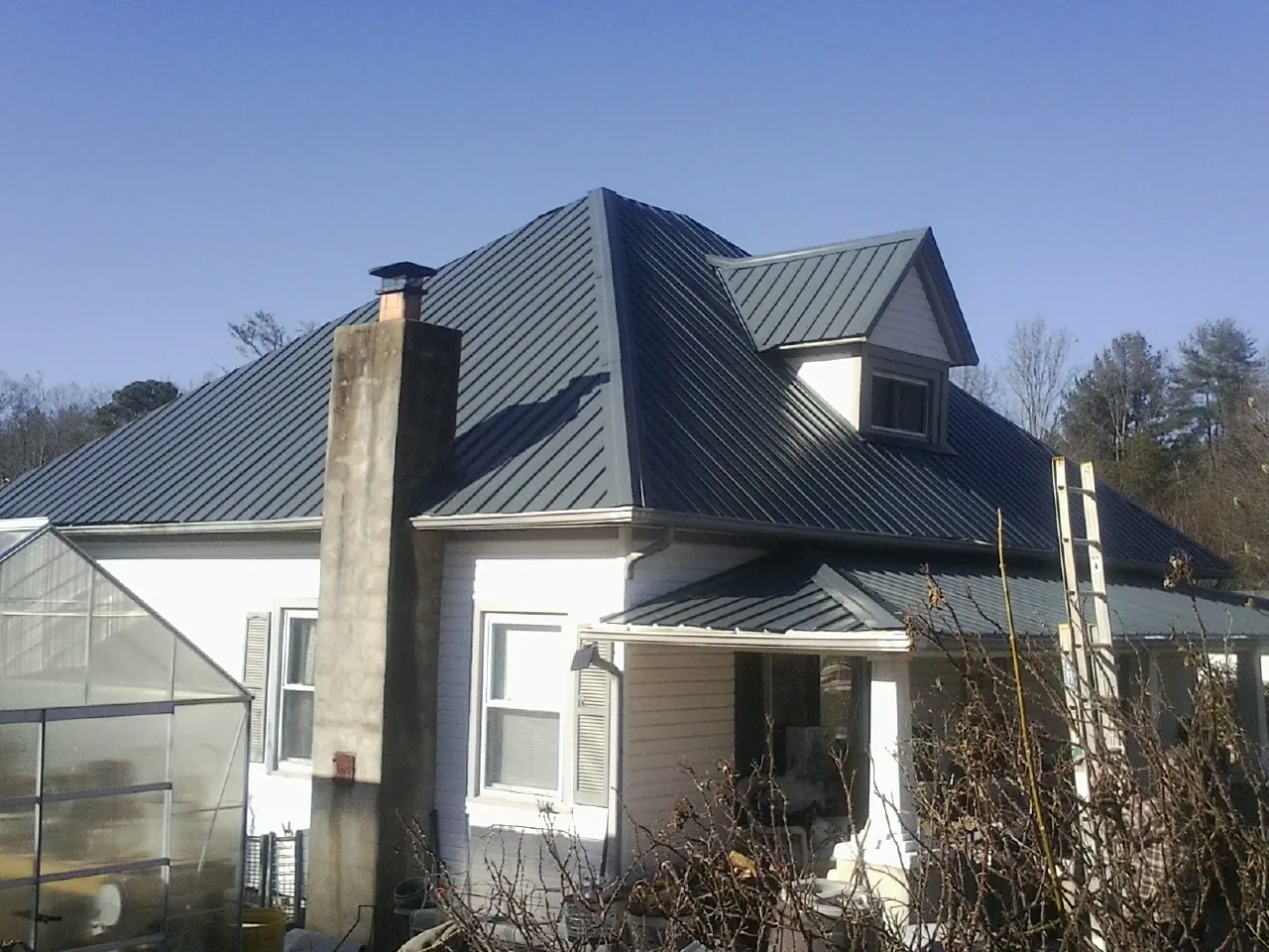 Dark blue standing seam metal roof on a white farmhouse with dormer — Slate & Tile Roof Repair by Roofing Brothers in Chestnut Hill