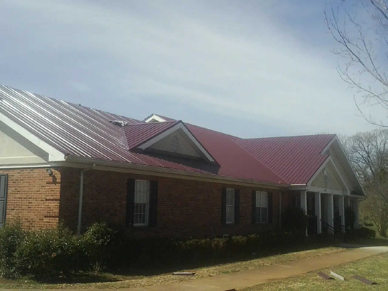 Red metal roof with gabled entries on a long brick building, from a Hail Damage Roof Repair job in Chestnut Hill