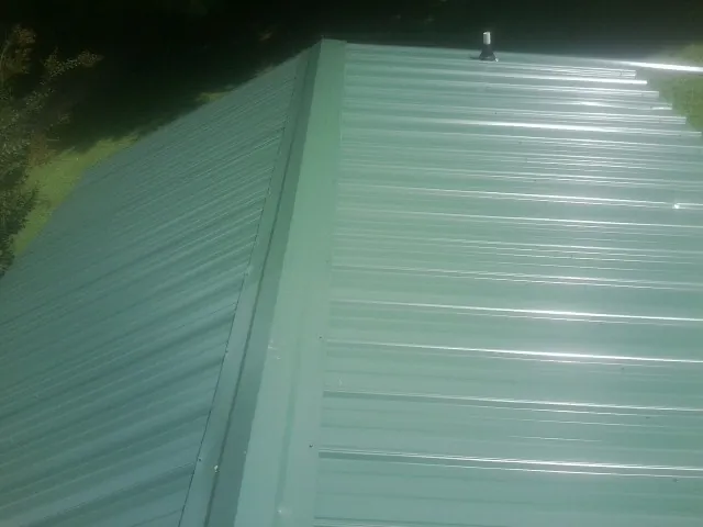 New green metal panels meeting at the ridge of a roof — Flat Roof Repair work by our crew in Chestnut Hill