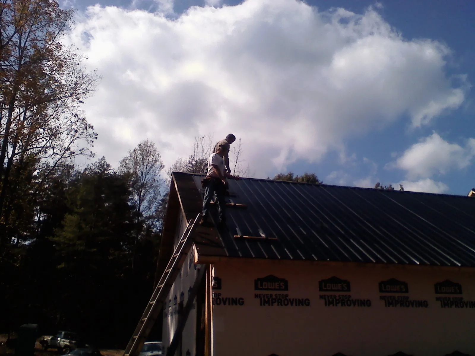 Roofer fastening dark metal panels high against a cloudy sky, from a Roof Inspection job in Chestnut Hill
