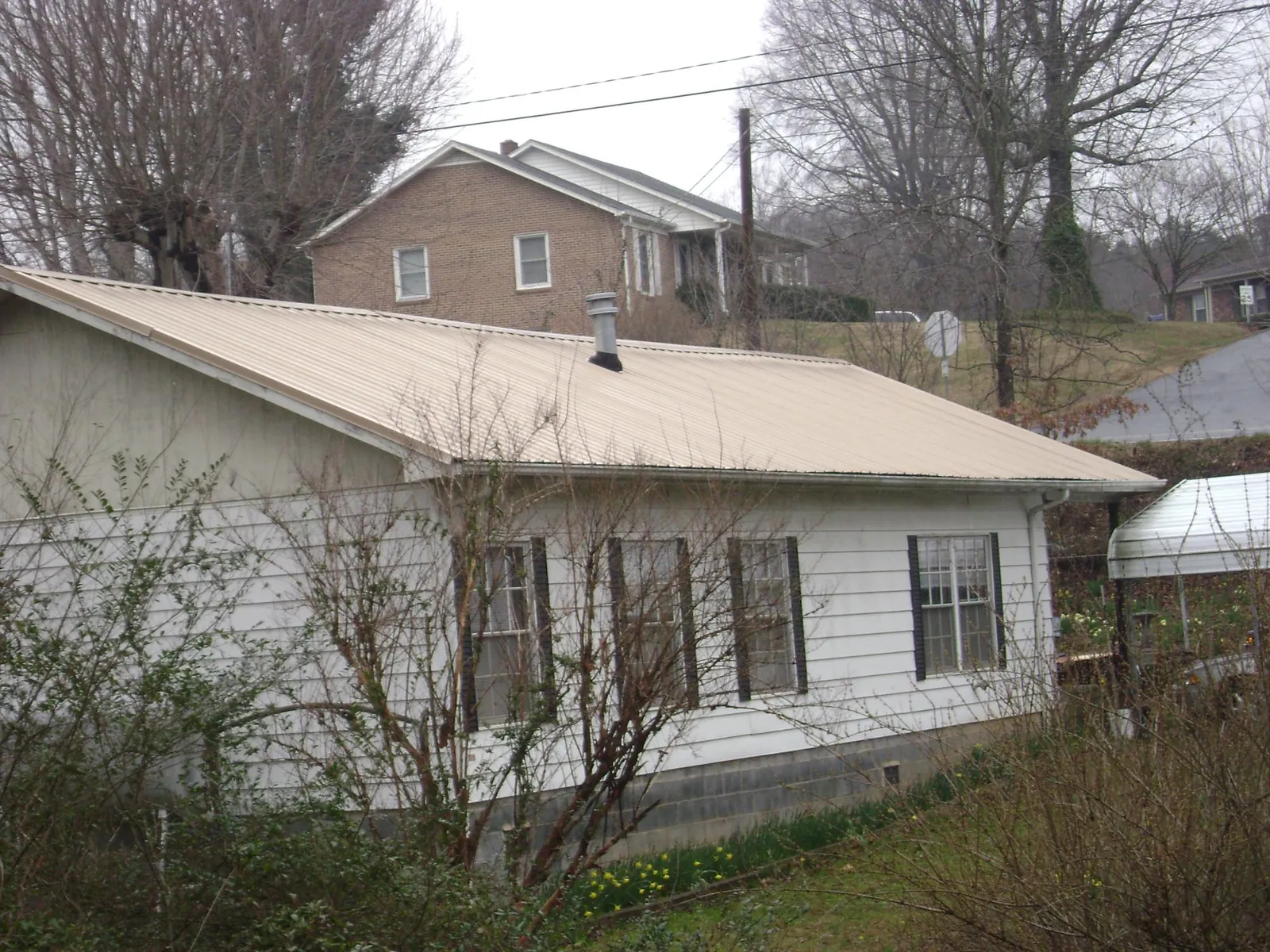 Tan metal roof on a white sided house set into a hillside — Commercial Roofing by Roofing Brothers in Chestnut Hill