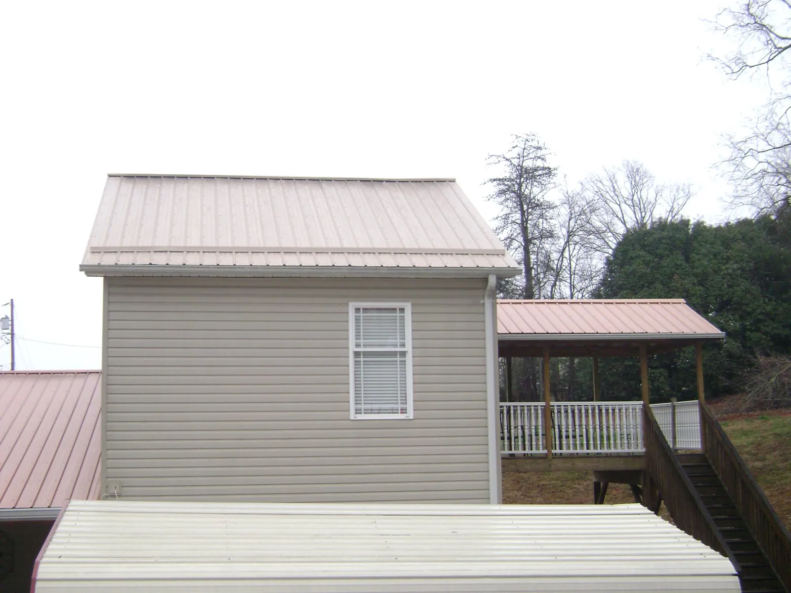 Tan metal roofs on a two story addition and attached porch, from a Roof Replacement job in Chestnut Hill